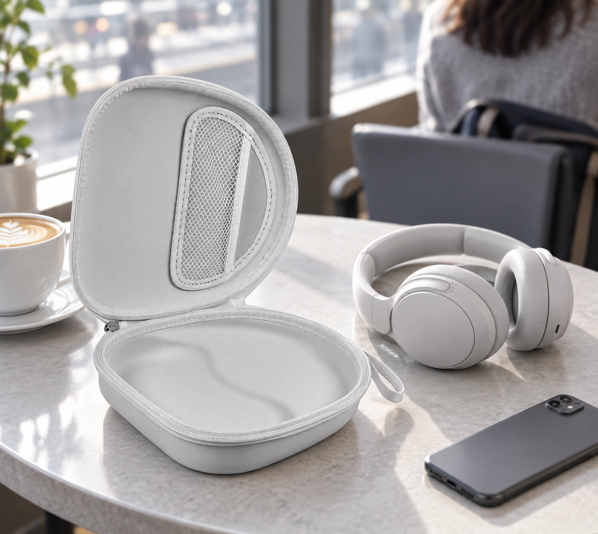 Open light gray ALKOO headphone case beside over-ear headphones on a cafe table