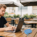 Blue portable SSD case beside a laptop at an outdoor cafe